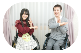 写真：いがりともかさんとインタビューアーの高橋豪さんが車いすに乗って、笑顔で一緒に仮面女子の決めポーズをしている様子