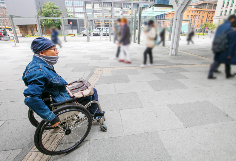 写真：車いす使用者が人ごみの歩道を移動する様子