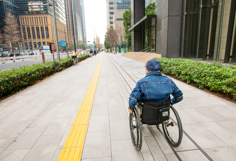 写真：車いす使用者が点字ブロックのある歩道をまっすぐ移動する様子