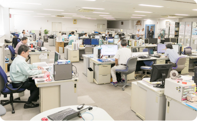 写真：幅広い通路が確保されたオフィスで、社員がパソコンに向かい仕事する様子