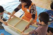 写真：塩山ファクトリーのスタッフの指示の元で園児たちが紙漉き作業を行っている様子