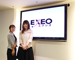 写真：インタビュアーと広報の女性2名がロゴの前に立っている様子