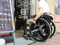 写真：車椅子を利用した社員が入店しようとしている様子。自動ドアは軽く触れると開くタイプ。