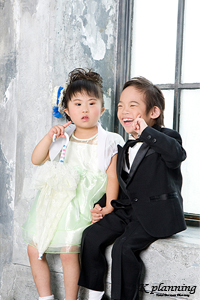 写真：男の子は黒のタキシードに女の子は白のドレスの姿で窓辺に座って笑顔でポーズをとっている写真