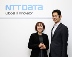 写真：インタビュアーと二人笑顔でNTTDaTaのロゴの前での記念写真