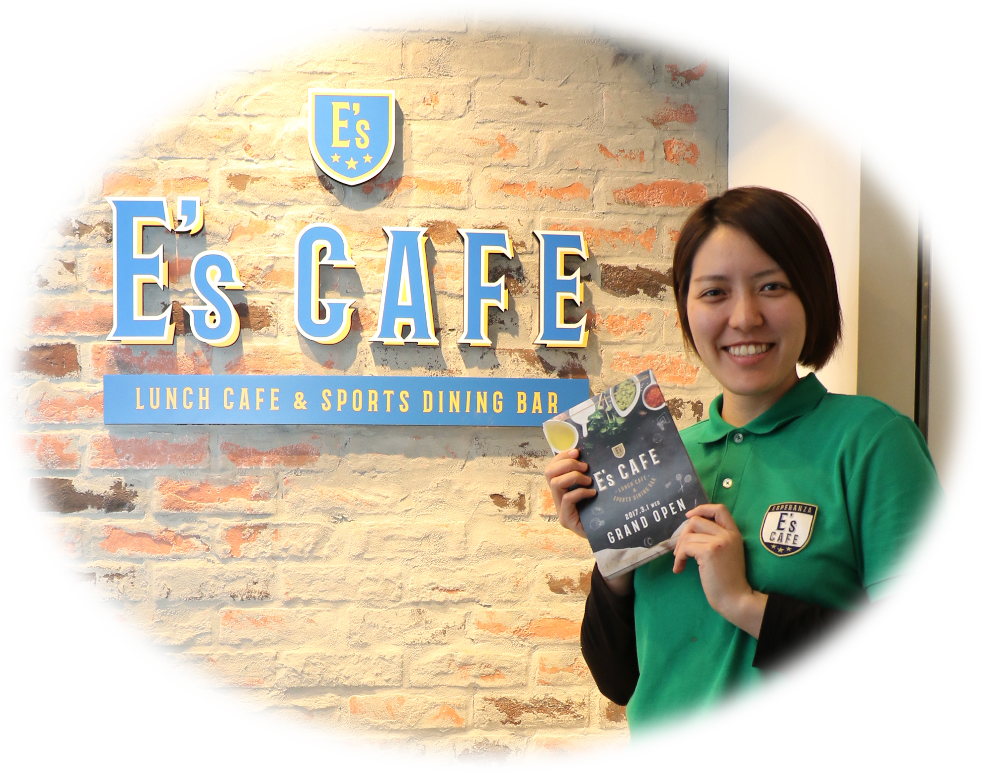 写真：Es' CAFEのロゴの前で微笑んでいるマネージャ