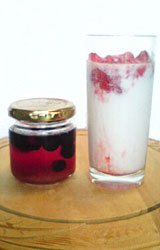 写真：赤い液体の果実酢（サワードリンク）が入った保存用の瓶（左）とそのサワードリンクを牛乳で割ってグラス(右)に注いである。