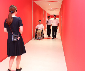 写真：ポッキーをイメージした赤い壁でスタッフの方から案内を受けている編集部員たちの様子。