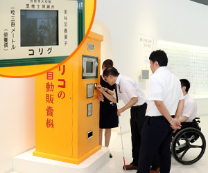 写真：復元された自動販売機にお金を入れている。左上に白黒映画のアップ