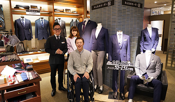 写真：5パターンのスーツを着たマネキンをバックに、編集部員と須藤ショップマネージャーと広報の方の集合写真