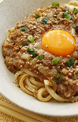 写真：お皿にできあがったキーマカレーうどんが盛られている。トッピングに白ごま、青ネギ、そして中央には卵の黄身が輝いている！