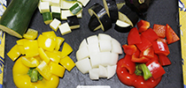 写真：まな板にズッキーニ、ナス、玉ねぎ、黄色と赤のパプリカが並べられている