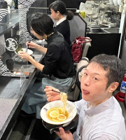 画像：車いすユーザの編集部員が手話通訳士と一緒にラーメンを食べている