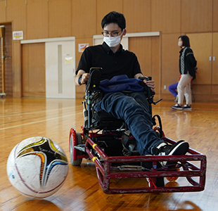 写真：電動車いすでボールを蹴る編集部員