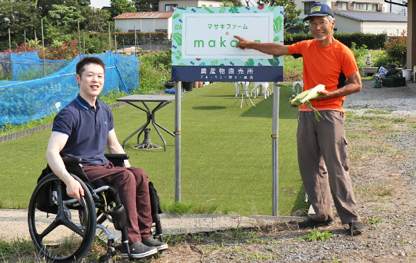 写真：マサキファームmakana（マカナ）の看板前で編集部員と正木さんのツーショット