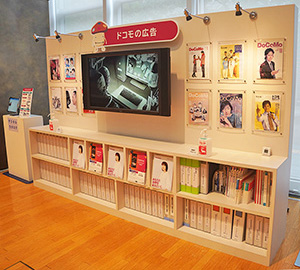 写真：壁掛けテレビでは最新のCMが流れていて、その下にある本棚には歴代の商品カタログがファイリングされて並んでいる