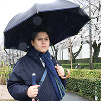 写真：雨の中、視覚障がいのある社員が左手にはサイレントアンブレラと右手には白杖を持っている