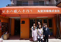 写真：日本の職人手作りと書かれた丸安洋傘株式会社の玄関前に社員が集合して立っている